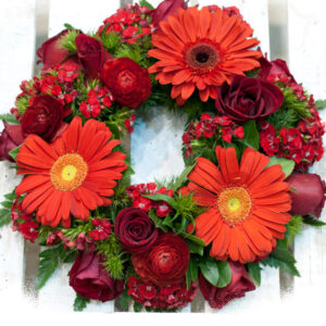 Σύνθεση λουλουδιών σε ειδική βάση με κόκκινα λουλούδια. Ζέρμπερες, γαρύφαλλο και τριαντάφυλλα αποτελούν αυτό το στεφάνι.
